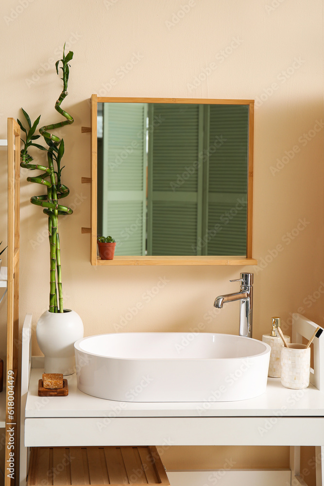 White sink, bath accessories and vase with bamboo stems on table in room