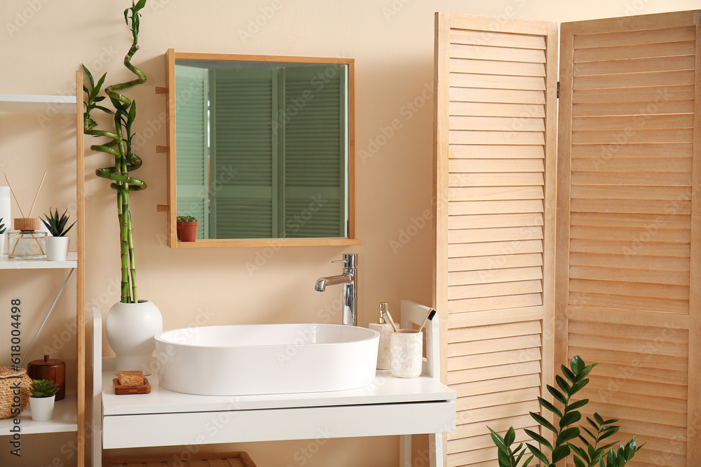 White sink, bath accessories and vase with bamboo stems on table in room