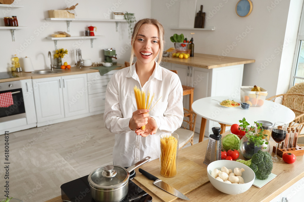 Young woman with raw pasta in kitchen