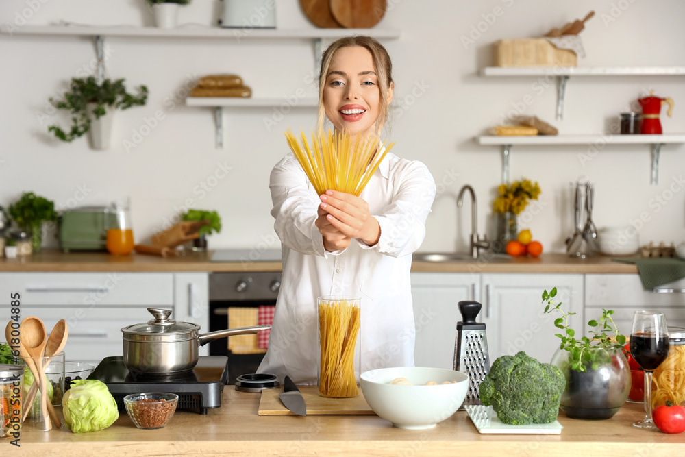 Young woman with raw pasta in kitchen