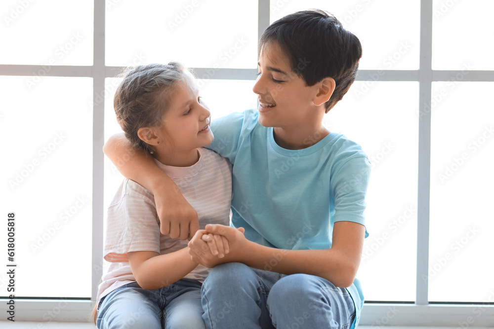 Little boy with his sister hugging near window