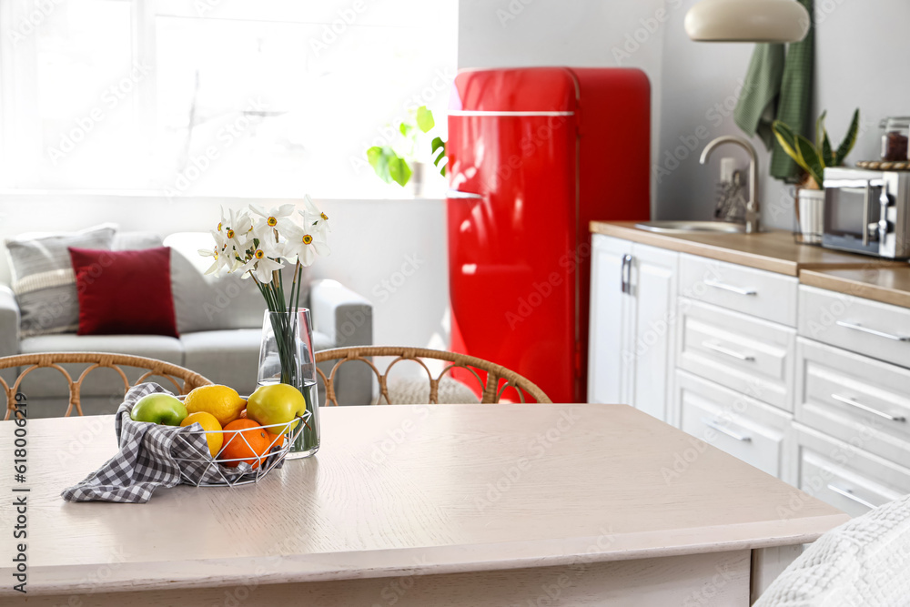 Basket with fruits and narcissus flowers on table in light kitchen, closeup