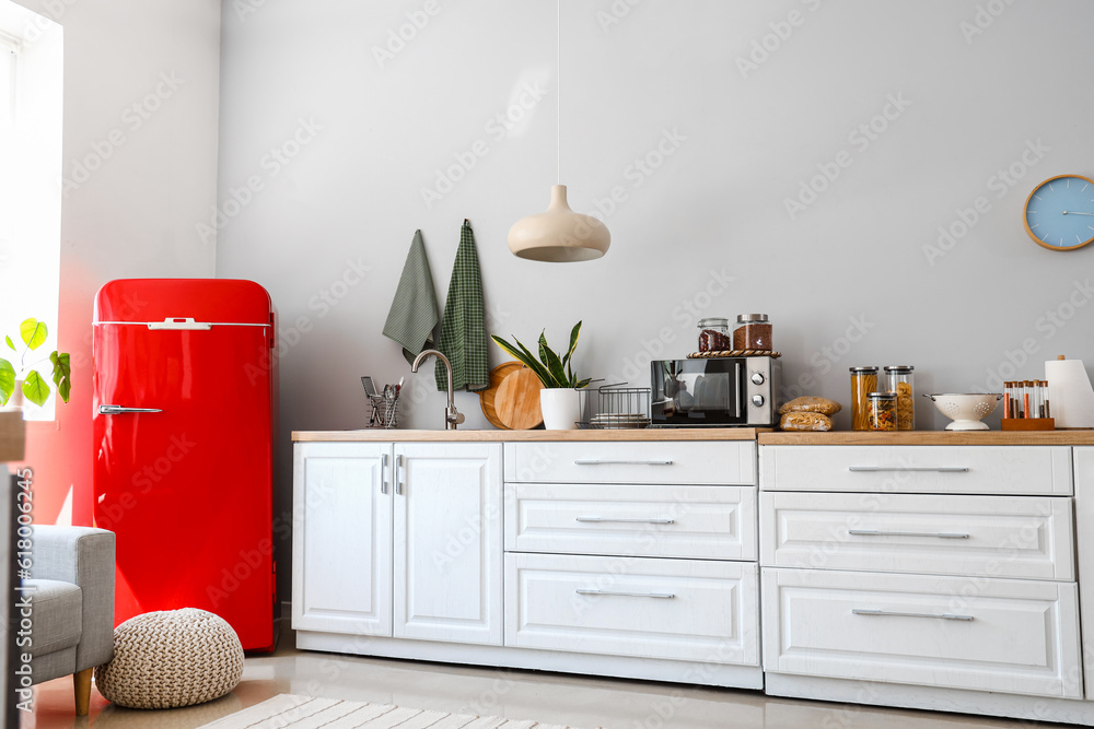 Interior of light kitchen with red fridge, counters and pouf