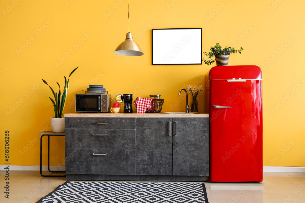 Interior of stylish kitchen with red fridge, counters, blank picture and houseplants