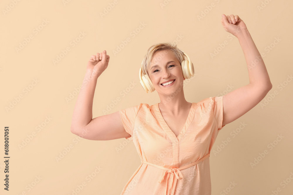 Mature woman in headphones dancing on beige background