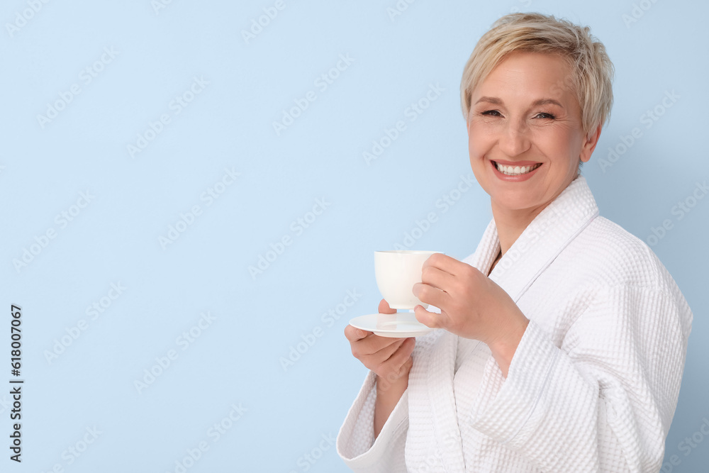 Mature woman in bathrobe with cup of coffee on blue background