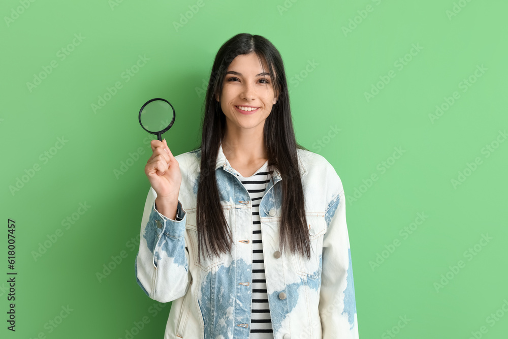 Beautiful happy young woman with magnifier on green background