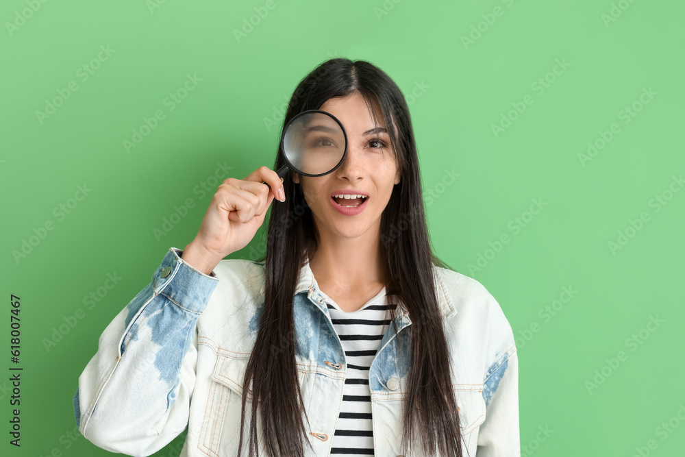 Beautiful excited young woman with magnifier on green background