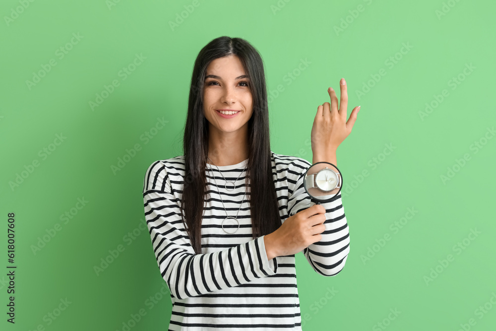 Beautiful happy young woman with magnifier and wristwatch on green background