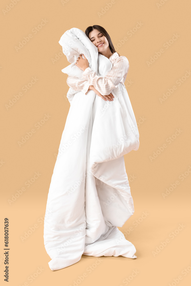 Beautiful happy young woman with soft blanket sleeping on pale orange background