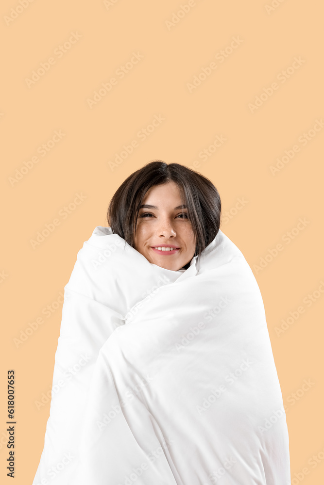 Beautiful happy young woman with soft blanket on pale orange background