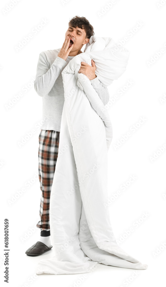 Handsome young man with soft blanket yawning on white background