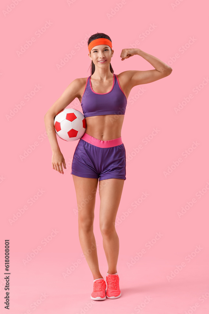 Sporty young woman with soccer ball on pink background