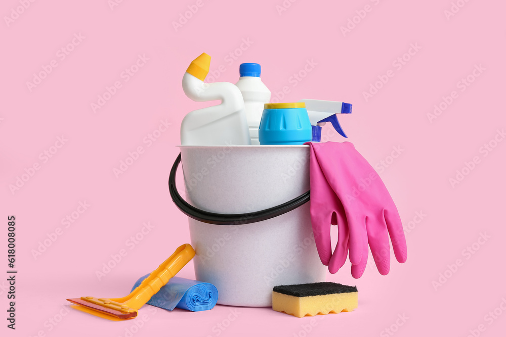 Bucket with different cleaning supplies on pink background