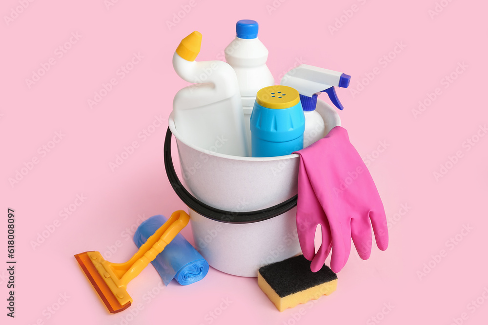 Bucket with different cleaning supplies on pink background