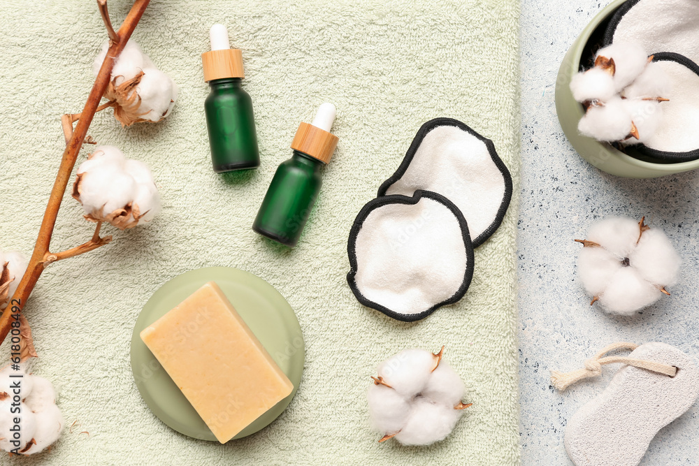 Bottles of essential oil, soap, clean towel, cotton flowers and pads on light background