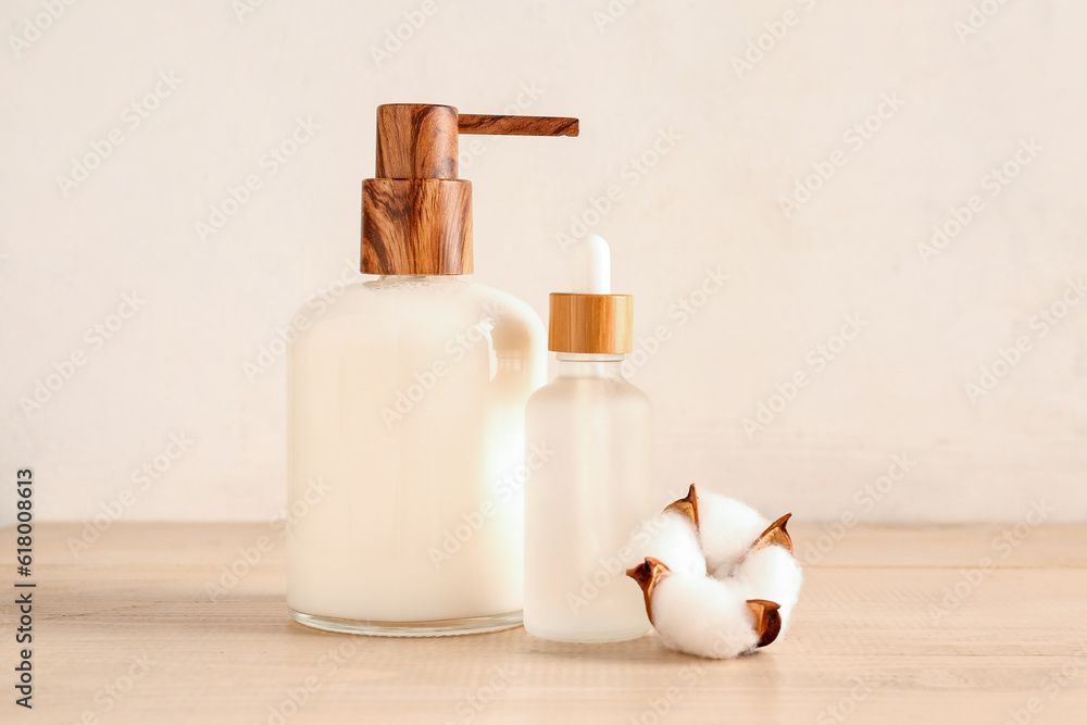 Bottles of cosmetic products and cotton flower on wooden background