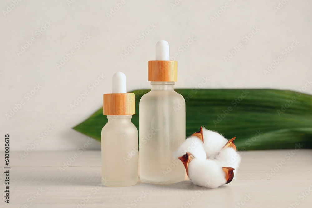 Bottles of essential oil and cotton flower on wooden background