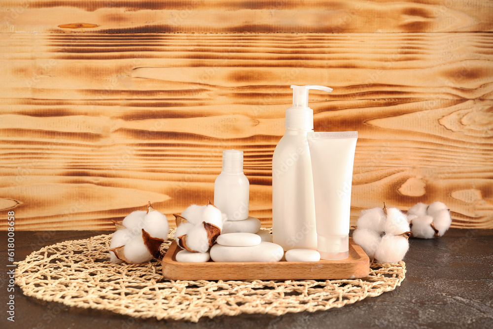 Bottles of cosmetic products, spa stones and cotton flowers on table against wooden background