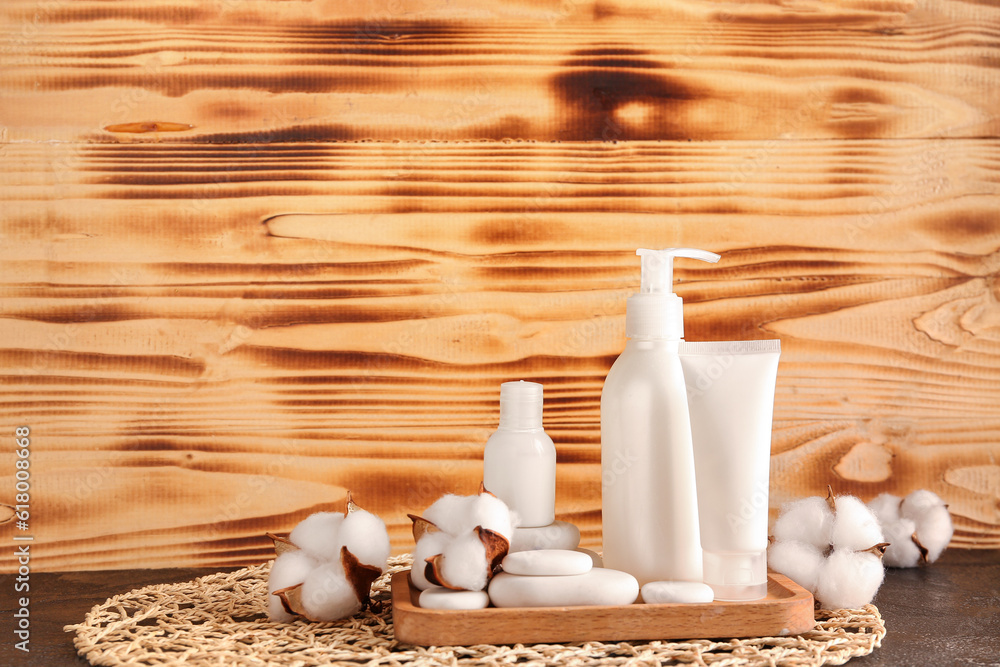 Bottles of cosmetic products, spa stones and cotton flowers on table against wooden background