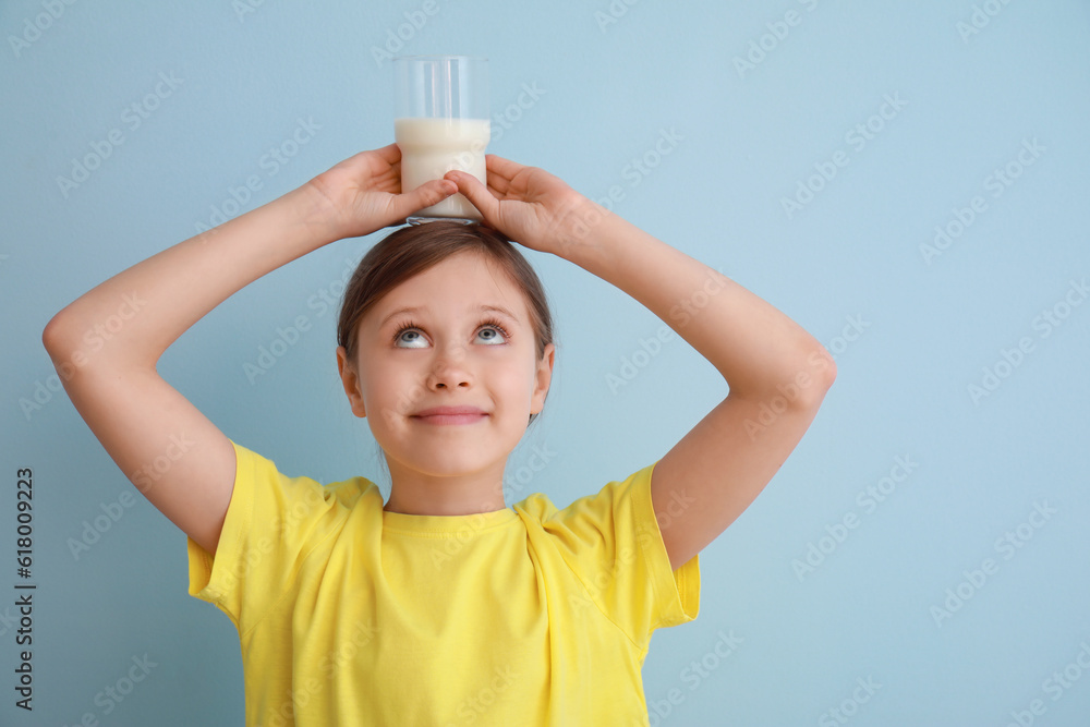 Little girl with glass of milk on light blue background