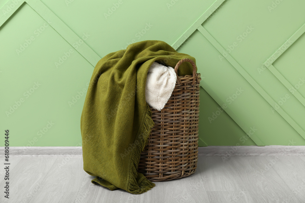 Basket with new soft blankets near green wall in room