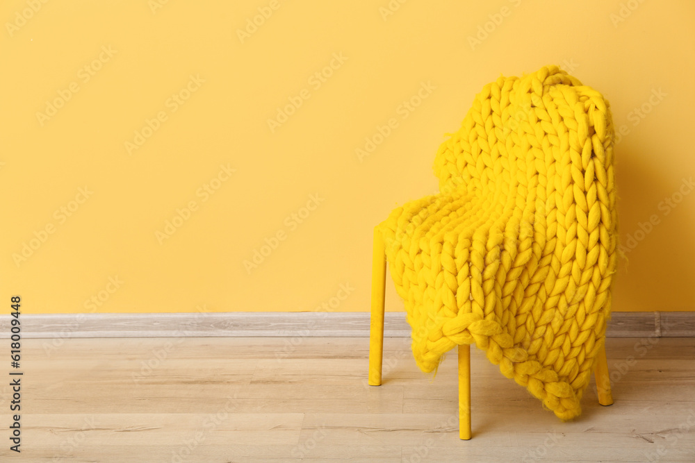 New knitted blanket on chair near yellow wall in room