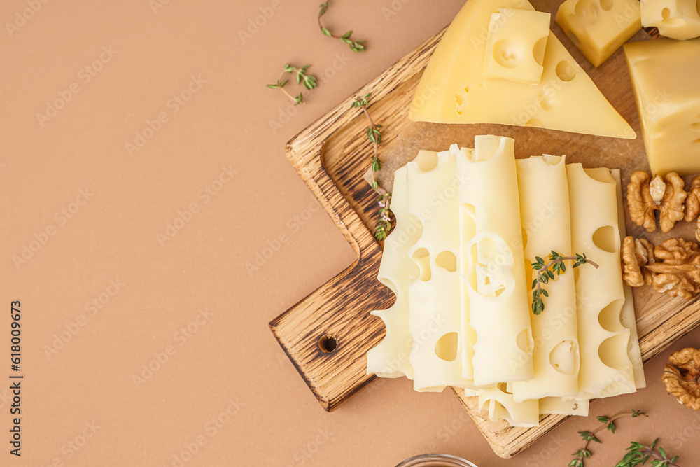 Board with pieces of Swiss cheese and walnut on brown background