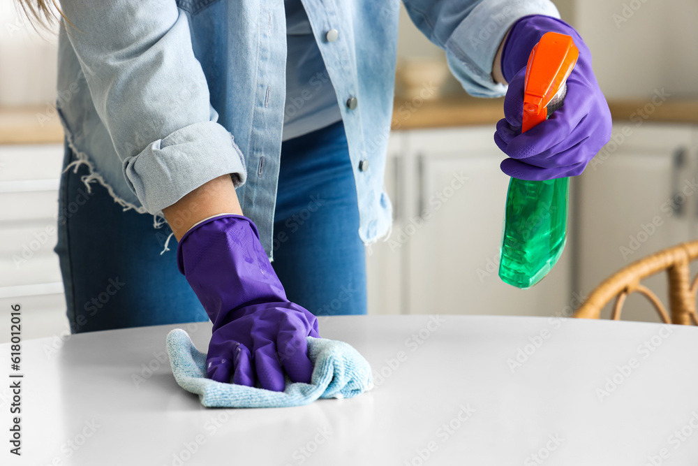 Woman in purple rubber gloves cleaning table with rag and detergent