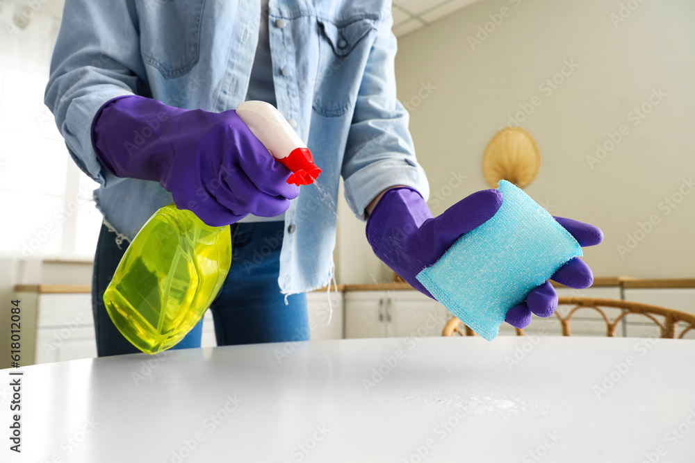 Woman in purple rubber gloves cleaning table with sponge and detergent