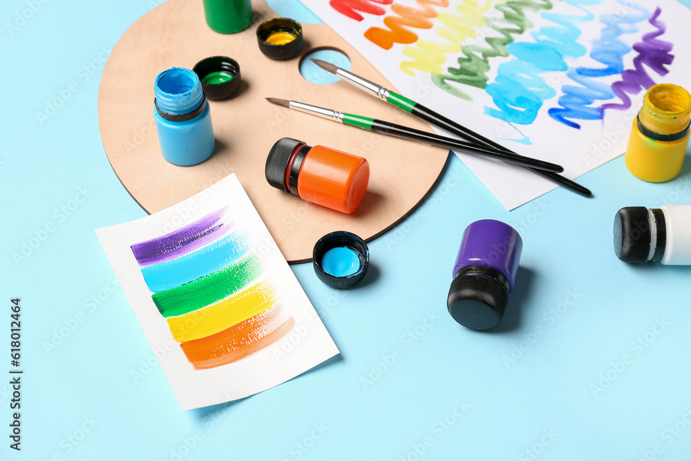 Composition with different paints, brushes and rainbow color palette on blue background