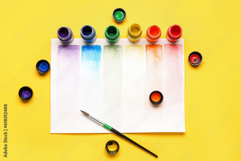 Composition with different paints, brush and rainbow color palette on yellow background