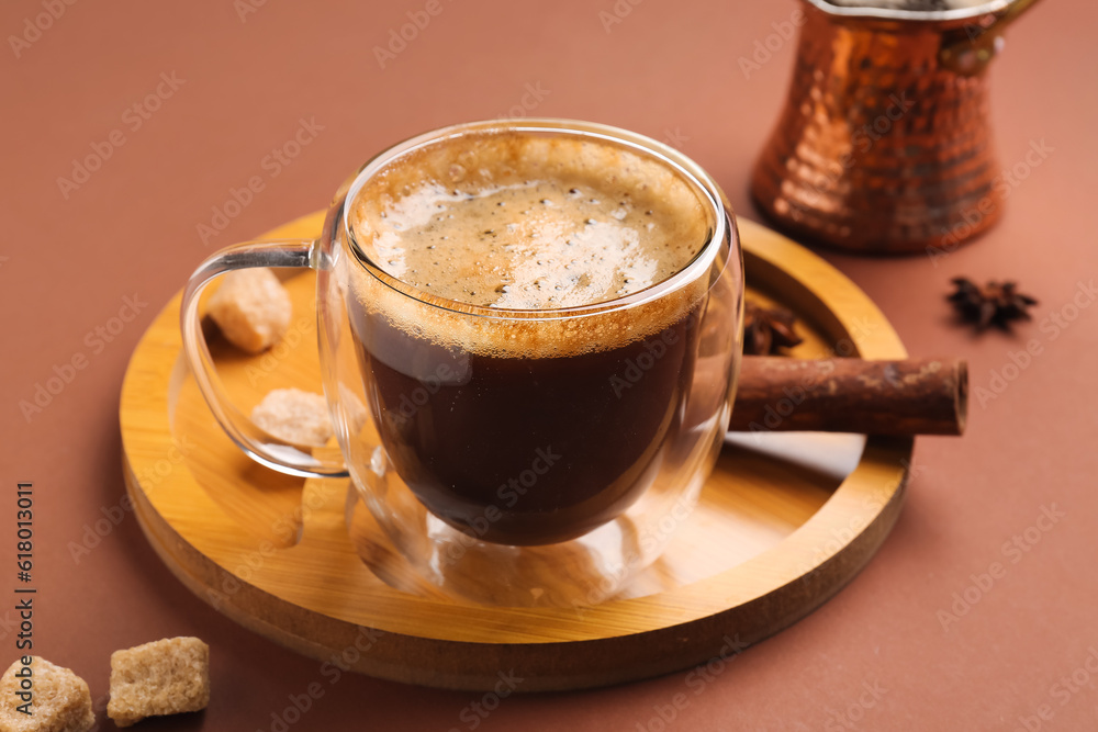 Board with glass cup and jezve of hot espresso on brown background