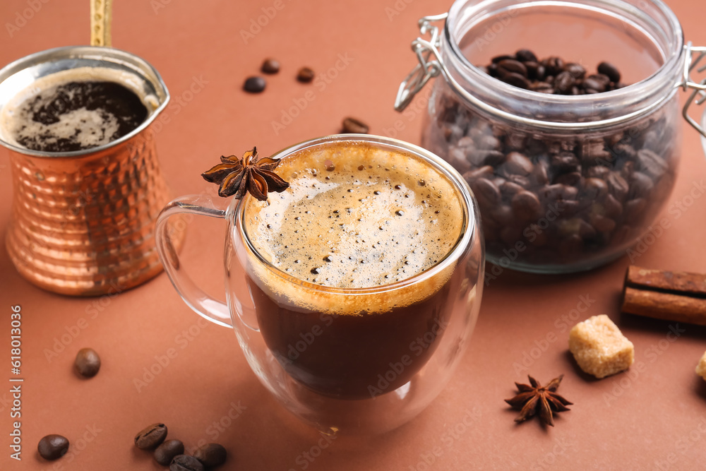 Glass cup and jezve of hot espresso on brown background