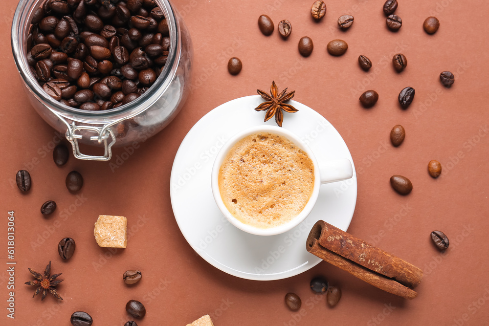 Cup of hot espresso and jar with coffee beans on brown background