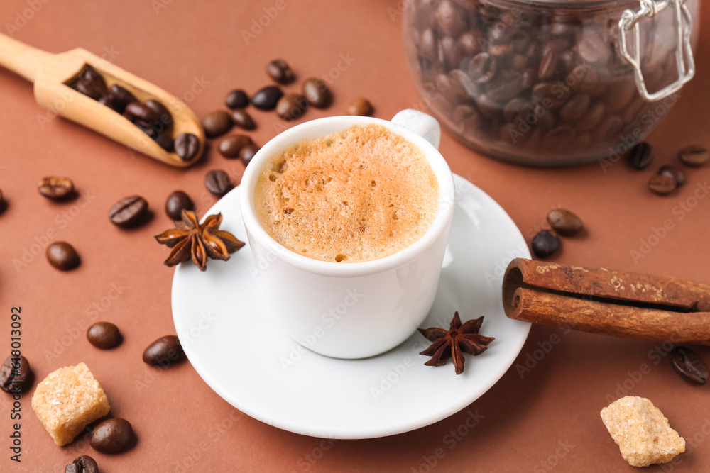 Cup of hot espresso and jar with coffee beans on brown background