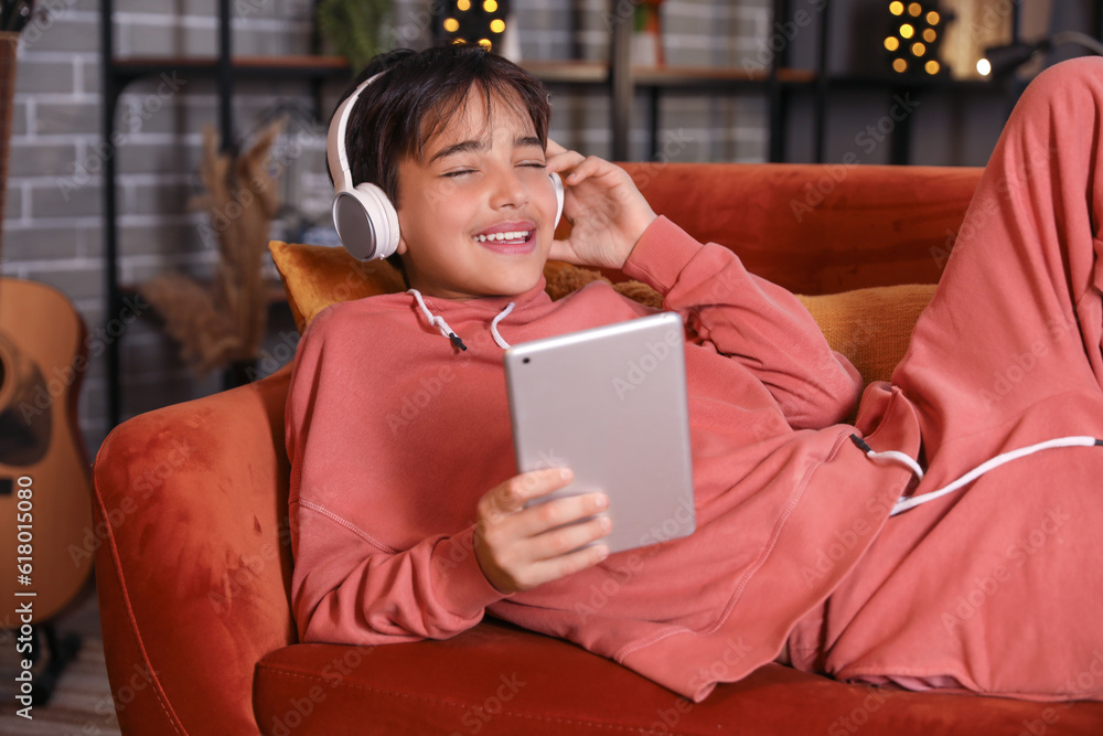 Little boy with headphones using tablet computer at home late in evening