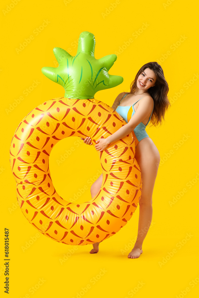 Young woman with swim ring in shape of pineapple on yellow background