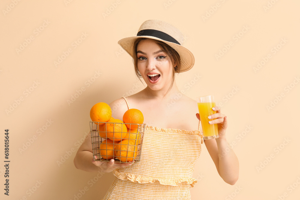 Young woman with glass of juice and oranges on beige background