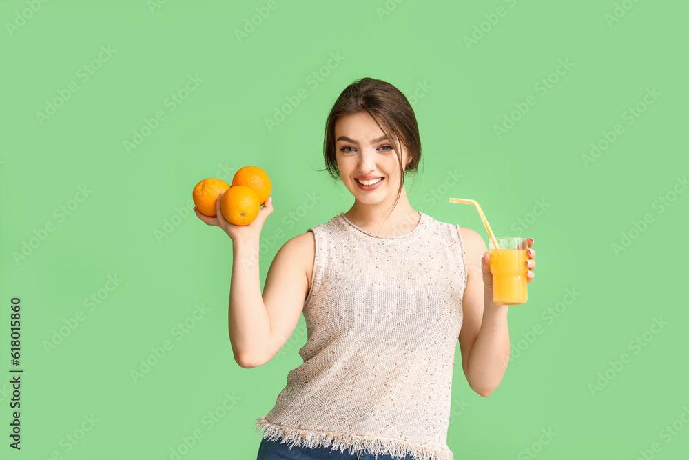 Young woman with glass of juice and oranges on green background