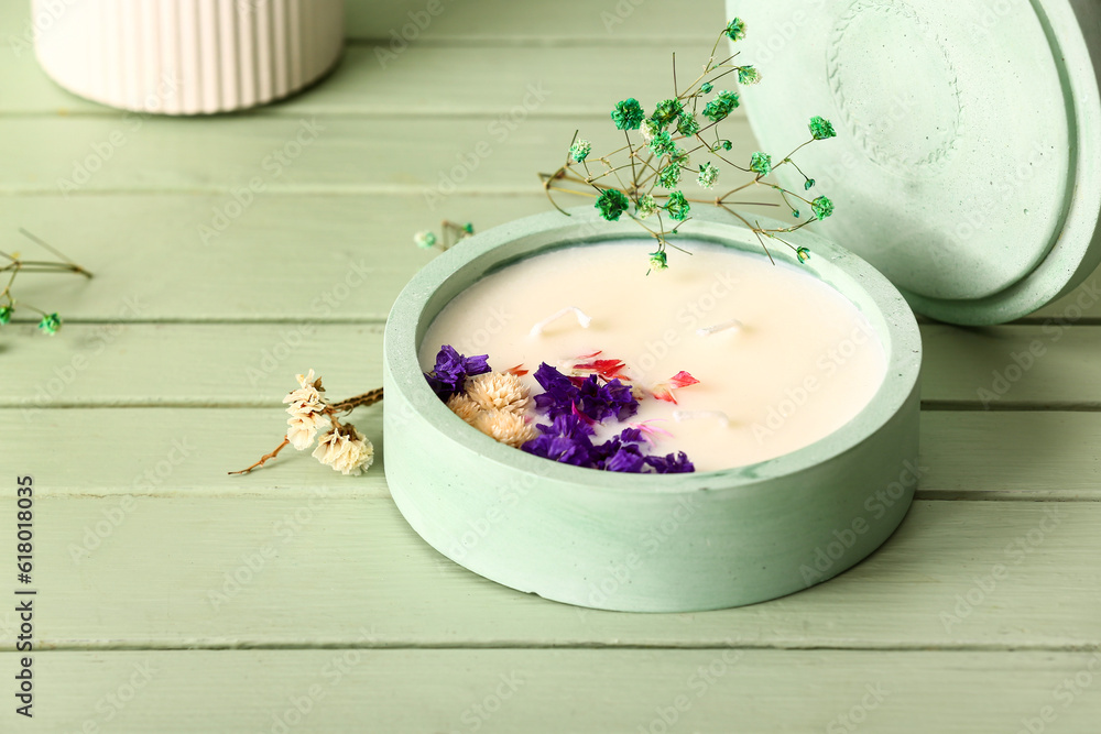 Holder with candle and flowers on green wooden background