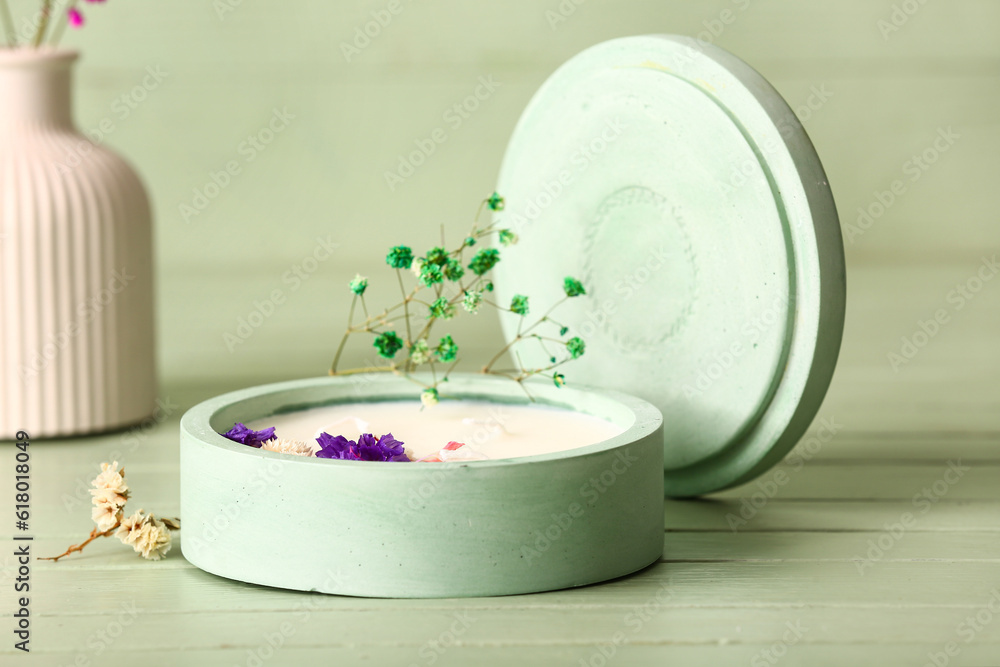 Holder with candle and flowers on green wooden background