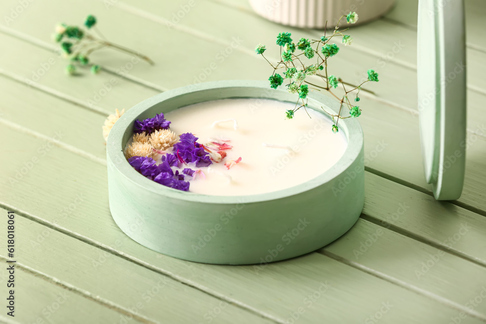 Holder with candle and flowers on green wooden background