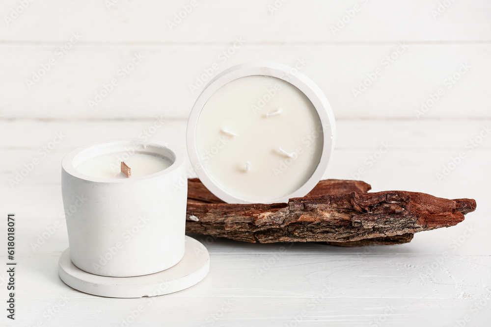 Holders with candles and tree bark on white wooden background