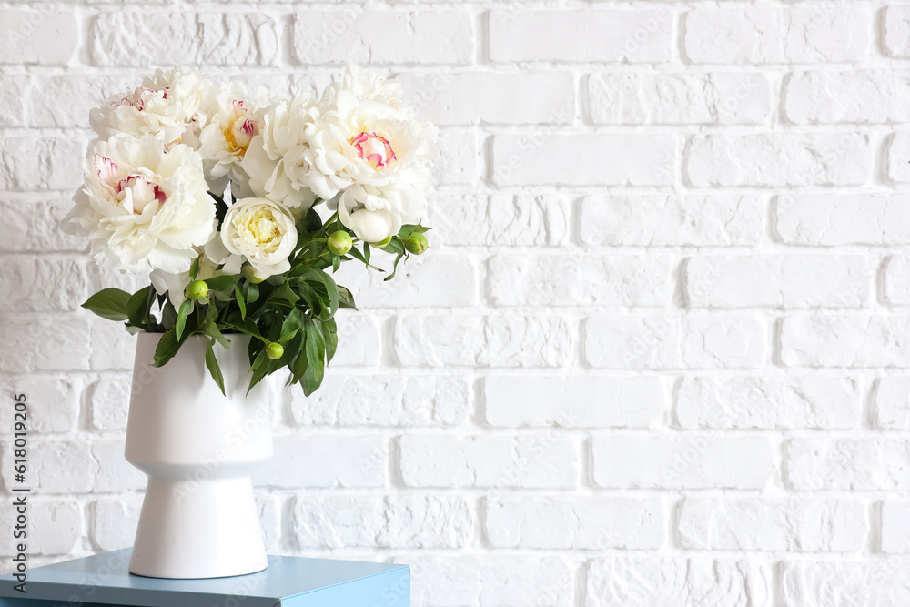 Vase of white peonies near brick wall