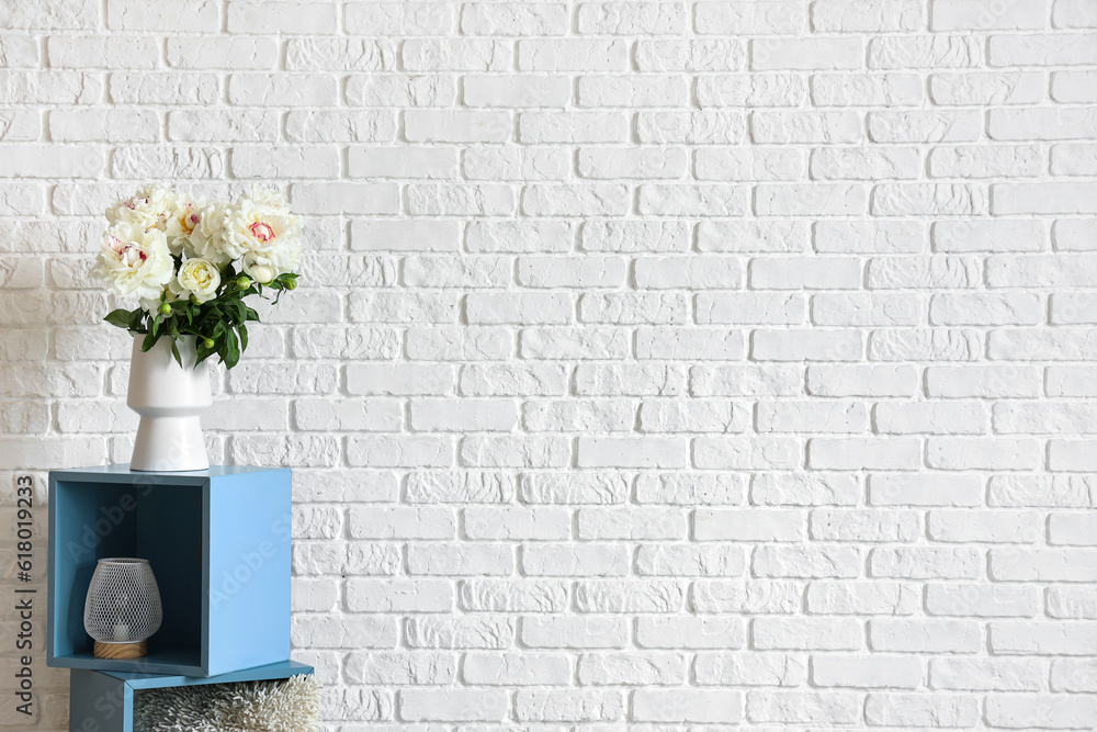 Vase of white peonies near brick wall