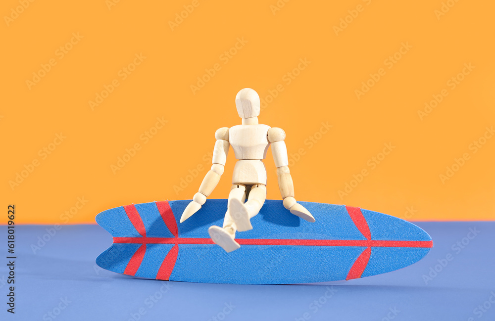 Mini surfboard with wooden mannequin on blue table against orange background