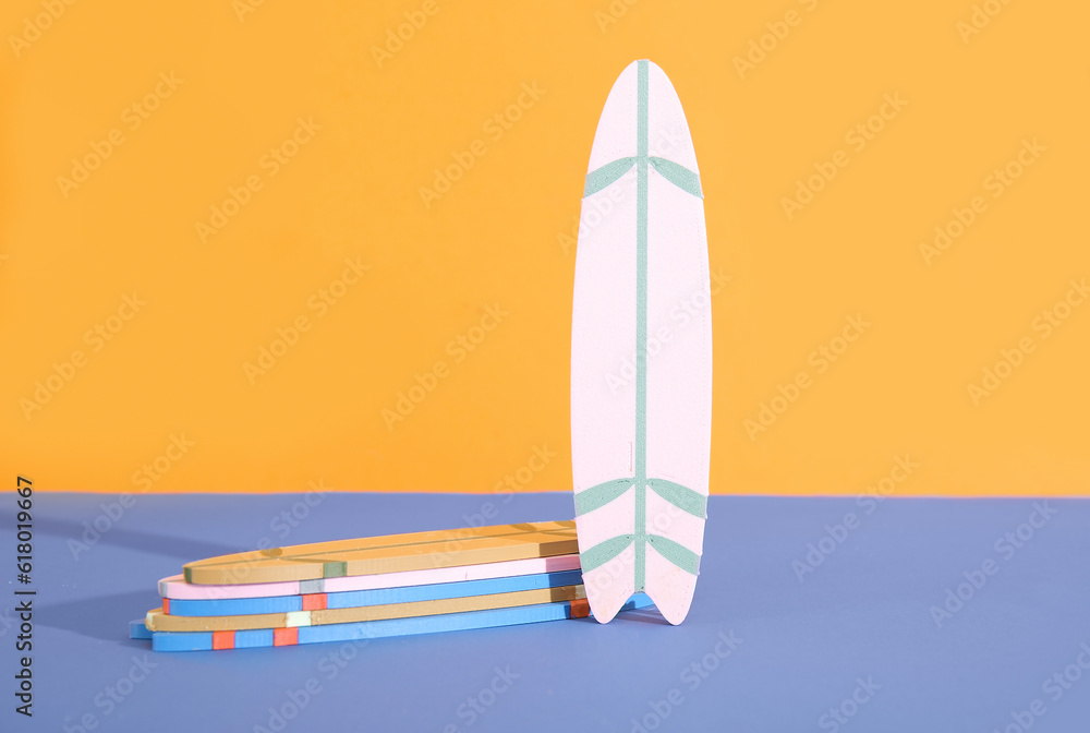 Many different colorful mini surfboards on blue table against orange background