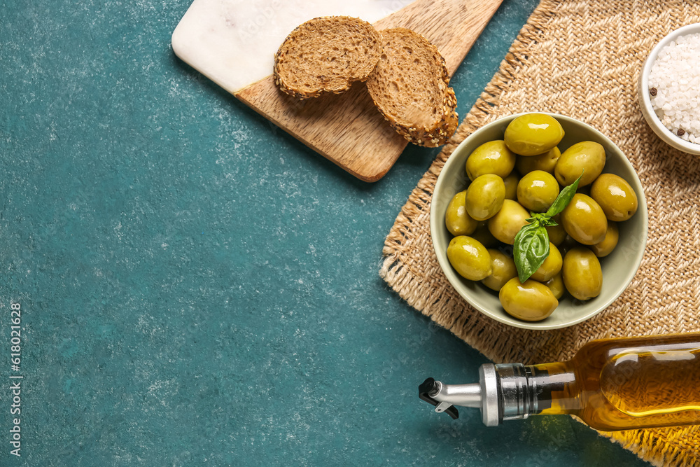 Bowl with ripe olives, bread and bottle of oil on green background