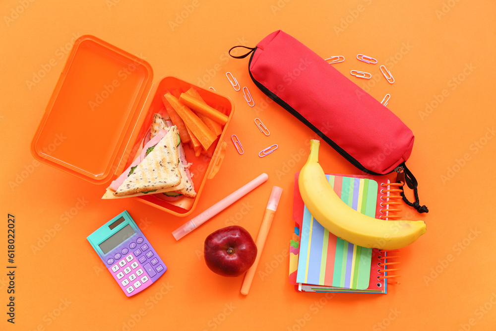 Different stationery and lunch box with tasty food on orange background